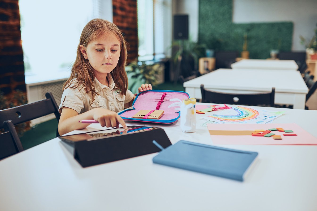 Schoolgirl using tablet. Child doing homework sitting at des